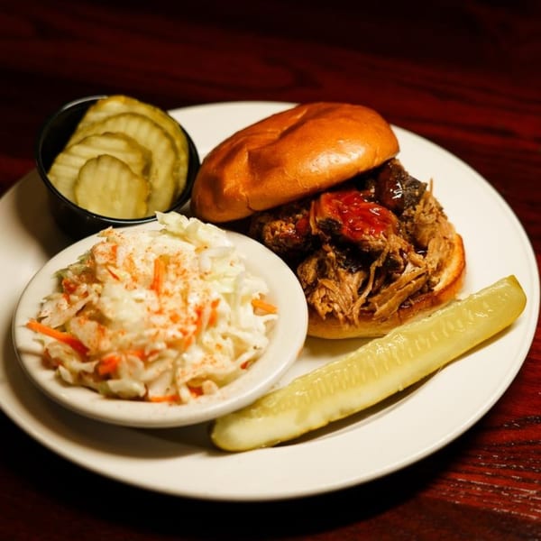 A Bullwinkle's BBQ pulled pork sandwich with coleslaw, pickle slices, and a pickle spear.