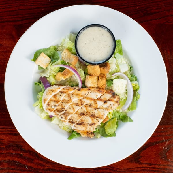Grilled chicken Caesar salad with croutons, red onion, and dressing on a white plate.