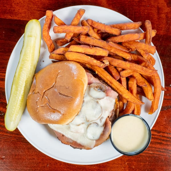 A Bullwinkle's BBQ sandwich with melted cheese and mushrooms, sweet potato fries, and a pickle spear.