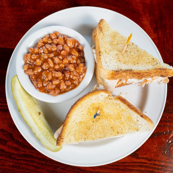 A Bullwinkle's Top Hat Bistro BBQ sandwich with baked beans and a pickle spear.