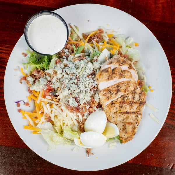 Grilled chicken salad with blue cheese, bacon, shredded cheese, hard-boiled eggs, and ranch dressing.