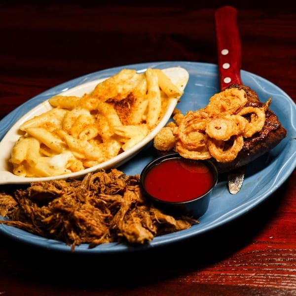 A blue plate with pulled pork, mac and cheese, BBQ ribs with onion rings, and a side of sauce.