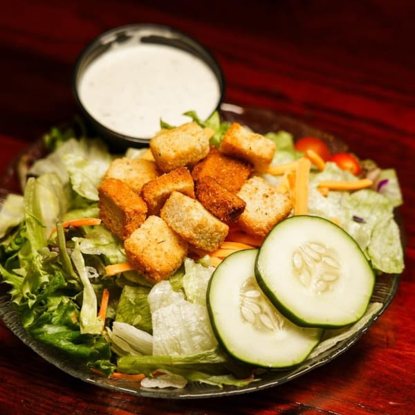 A fresh side salad with lettuce, cucumbers, croutons, and a side of ranch dressing.