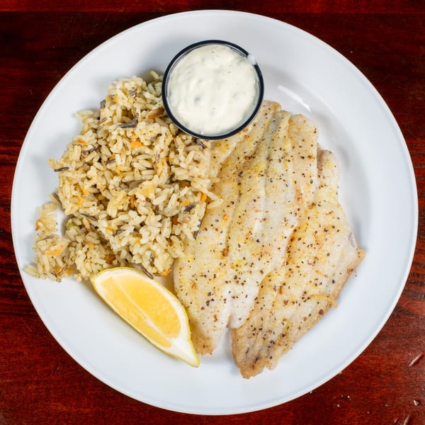 Grilled fish fillet with rice pilaf, a lemon wedge, and tartar sauce on a white plate.